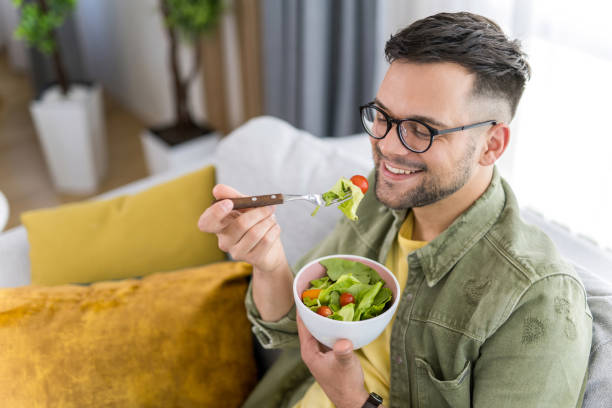 istock Young man eating a salad while relaxing on sofa. 1341836557