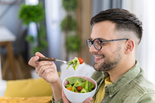 istock Young man eating a salad while relaxing on sofa. 1341836691