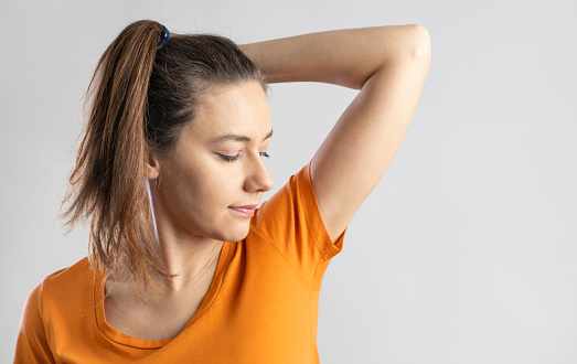 Young woman smelling her underarms in studio gray background