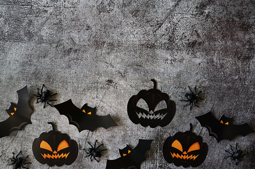Stock photo showing a Halloween poster / background design with homemade cut out bats and pumpkin Jack O'lantern shapes and spiders on black background, with copy space.