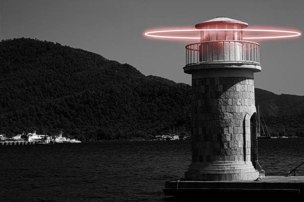 Picturesque red and white striped lighthouse on a grassy shore by the sea, with trees, blue sky, and calm water, perfect for travel, maritime, and coastal landscape themes.