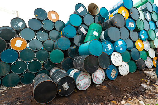 CHACHOENGSAO, THAILAND-JUNE 24, 2021 : Old chemical barrels stacked. Steel tank of plasticizer with label. Blue, green, black, and yellow chemicals barrels. Industrial drum. Hazard waste in factory.