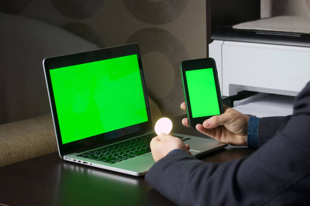 istock A man works at a laptop with a green screen. He holds a smartphone with a green screen and a cryptocurrency coin in his hand. Chromakey. 1341844310