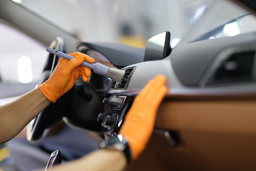 Male repairman cleaning air duct of car with brush closeup. Dry cleaning of car interior concept