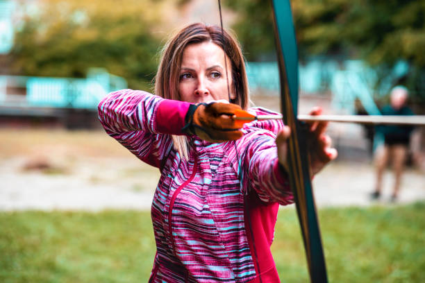 Mature woman shooting bow outdoors on autumn day