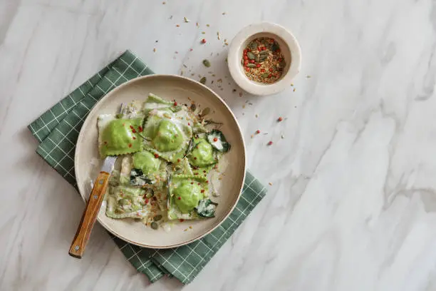 Vegan spinach ravioli, nuts, seeds and herb sauce. Flat lay top-down composition on marble background.