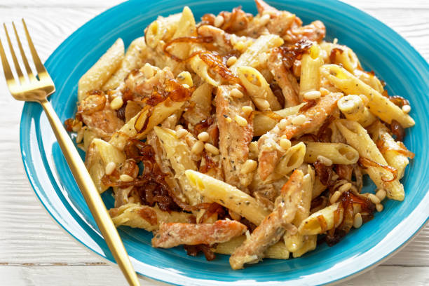 istock chicken alfredo pasta penne with caramelized onion sprinkled with pine nuts and grated parmesan cheese on a blue plate on white wooden table, close-up 1341850492