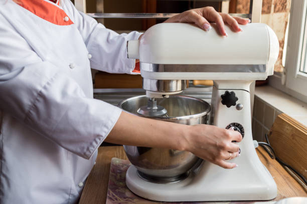 Young woman using kitchen mixer preparing dough for bread or sweet cake cream Young woman using kitchen mixer preparing dough for bread or sweet cake cream electric whisk stock pictures, royalty-free photos & images