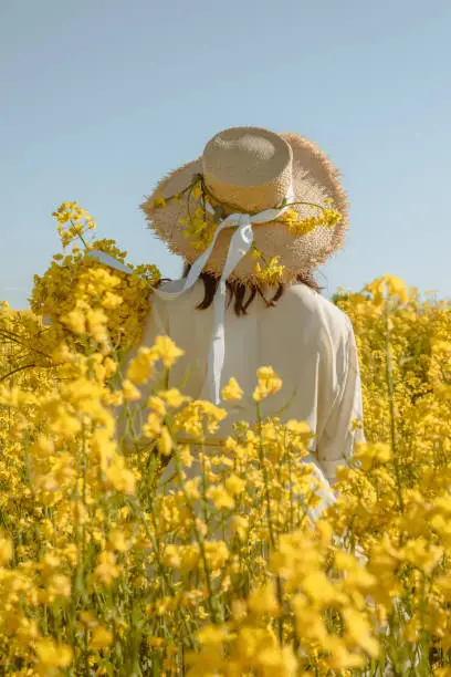 Photo of woman standing in rapeseed field rear view from behind