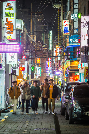 Young people strolling through the neon drenched night streets of downtown Seoul, South Korea.