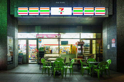 7 Eleven convenience store with plastic furniture outside for customers to use illuminated at night in central Seoul, South Korea.