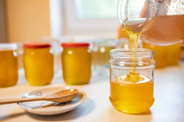 istock Someone pours honey into transparent jars on a white table 1341858255