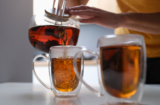 Woman pouring black tea from teapot into cup closeup. Family tea party concept