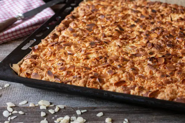 Homemade fresh baked sheet cake with crumbles and almonds served hot an a baking sheet on wooden table. Closeup and isolated view with blurred background