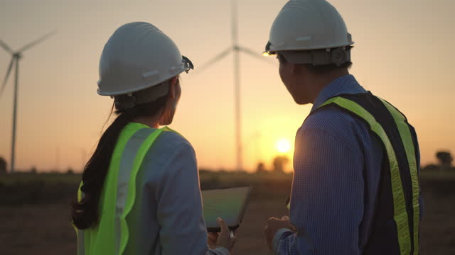 Two engineer using a digital tablet while working together in wind turbine farm