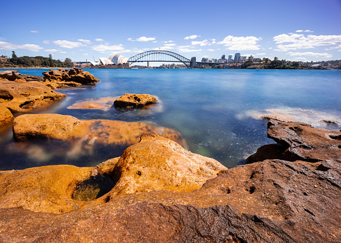 Sydney Harbour with nice rocks in the foreground the soft waves crashing on the shore and the beautiful harbour foreshore as a backdrop NSW Australia