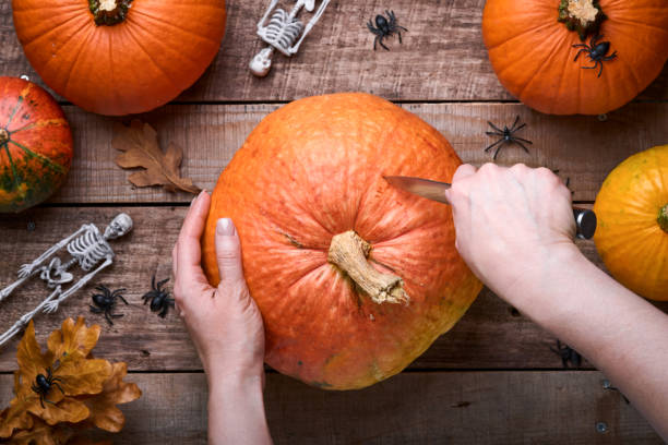 istock Halloween Pumpkin. Process female hands cutting with knife character face on pumpkin object preparation to halloween holiday on old wooden background. Flat lay autumn composition with copy space 1341866115