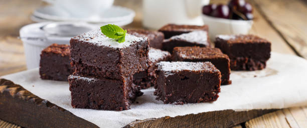 Chocolate brownies with powdered sugar and cherries on a dark wooden background. Selective focus. stock photo