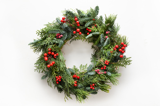 Festive Christmas wreath of fresh natural spruce branches with red holly berries isolated on white background. New Year. Top view. Traditional decoration for Xmas holiday.