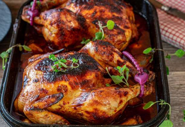 Spicy roast chicken with garlic honey sauce Delicious spicy dish with roasted whole chicken in a tasty garlic honey sauce served in baking dish on wooden table. Closeup view from above comprehensive stock pictures, royalty-free photos & images