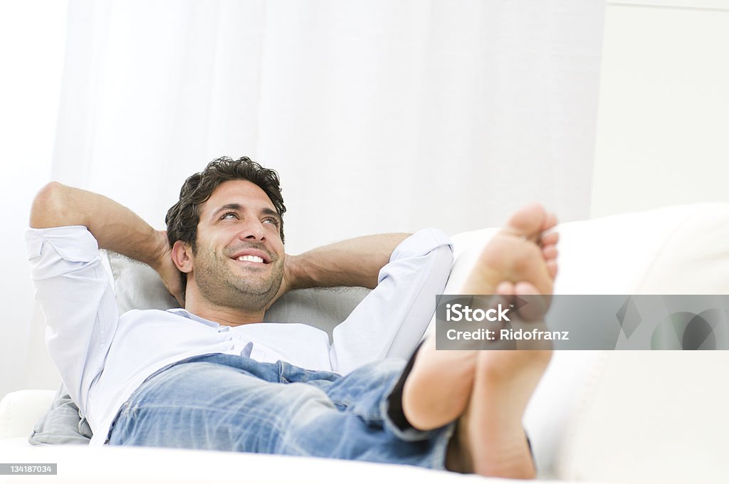 Dreaming and relax Smiling young man relaxing and dreaming on sofa at home. Lying Down Stock Photo