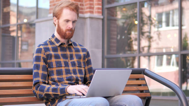 istock Redhead Beard Young Man working on Laptop, Sitting Outdoor on Bench 1341876152