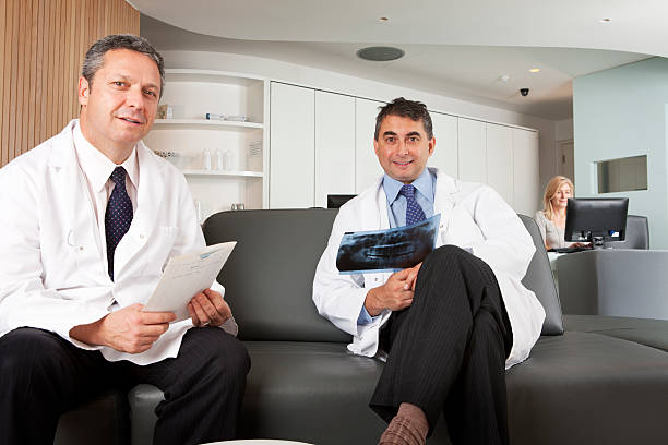 Two dentist sit on leather lounge to review X-rays stock photo