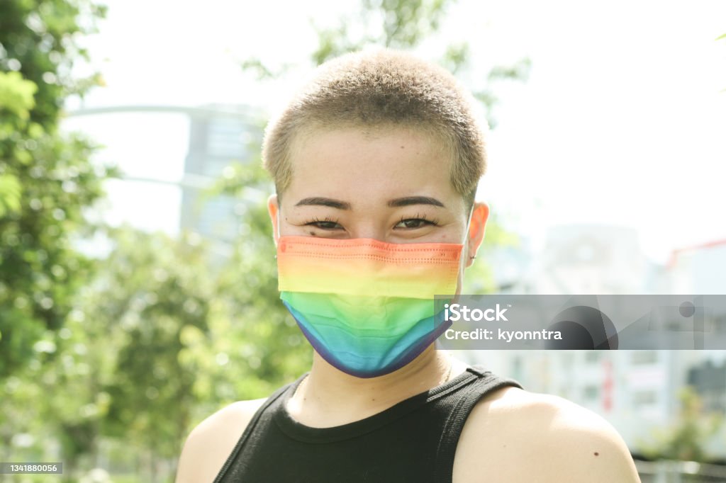 Asian buzz cut woman wearing a Rainbow Mask LGBTQIA＋ Concepts: Asian woman wearing a pride rainbow mask at outdoor. LGBTQIA People Stock Photo