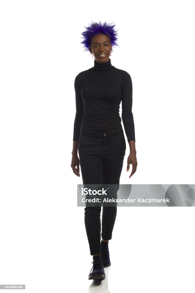 African American Woman In Black Clothes Is Walking Towards Camera. Full Length, Front View, Isolated Young smiling african american woman in black clothes and sneakers is walking towards camera. Front view. Full length studio shot isolated on white. Walking Stock Photo