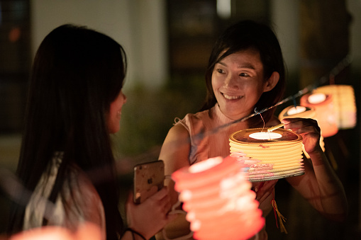 Asian Chinese mother and daughter light up candle in the paper lantern, celebration mid autumn festival.