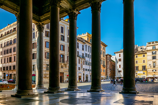 A suggestive view of Piazza della Rotonda from under the colonnade of the Roman Pantheon, in the historic and baroque heart of the Eternal City. Built in 27 BC by the Consul Marco Vispanio Agrippa for the emperor Augustus and dedicated to all the Roman divinities, the majestic Pantheon is one of the best preserved Roman structures in the world. Currently owned by the Italian state, this Roman temple preserves the remains of some Italian royalty and the Renaissance painter Raphael. In 1980 the historic center of Rome was declared a World Heritage Site by Unesco. Image in high definition format.
