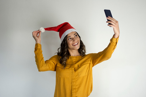 Young beautiful woman wearing christmas hat and taking a selfie isolated on white background