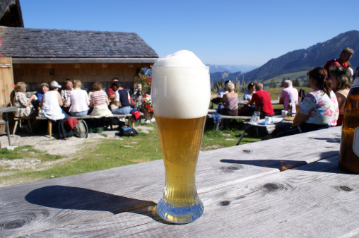 Focus on the beer. The cold, tasty, Bavarian wheat beer. Hikers gather in the background enjoying a mid-day snack and Alpine panorama atop Austria's Postalm in the Salzkammergut region.