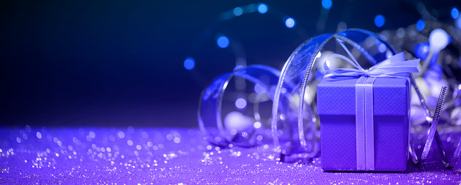 Close-up of a Christmas present (gift box) with defocused christmas lights and decorations in the background. Space for copy.