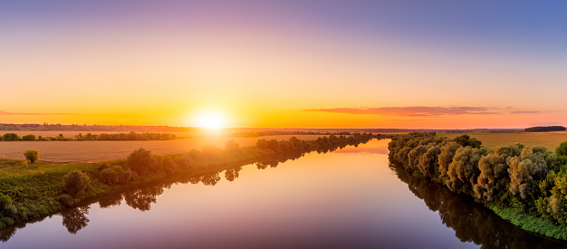 A sunset or sunrise scene over a lake or river with skies reflecting in the water on a summer evening or morning. Landscape.