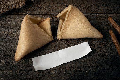 Cracked fortune cookie with an empty piece of paper on a wooden table