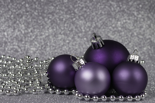four purple Christmas balls on a shiny silver background with silver beads. christmas composition