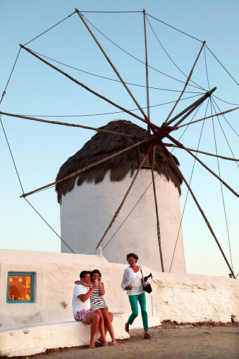 Mykonos, Greece - June 29: Group of people posing in front of a windmill on June 29, 2012 in Mykonos, Greece. Windmills from the 16th century, they are one of the most recognized landmarks of Mykonos.