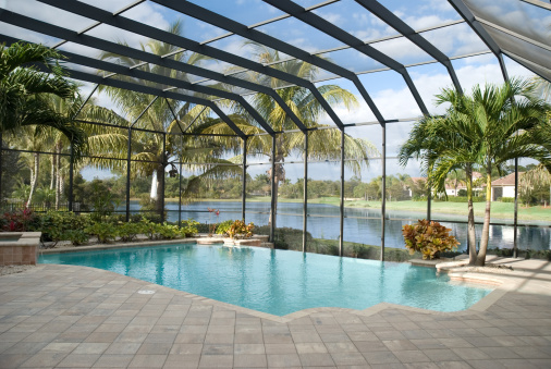 A backyard pool located in a tropical setting covered by a screen lanai. Lake in behind.