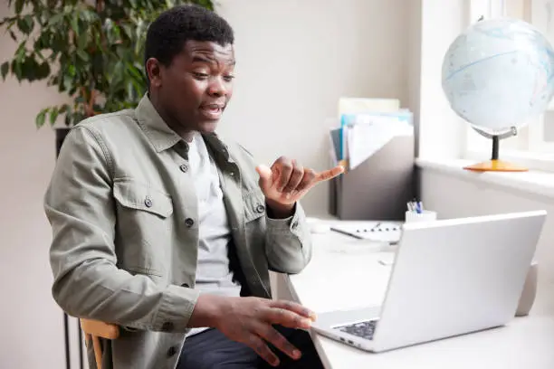 Young Man Having Conversation Using Sign Language On Laptop At Home