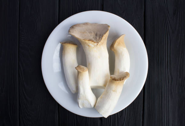 Mushrooms eringi in the white plate on the black wooden background. Top view. Close-up.