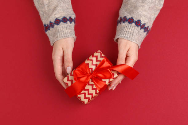 istock Female hands with christmas gift on red background, top view, copy space 1341905446