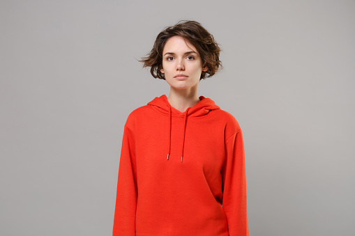 Attractive beautiful young brunette woman girl in casual red hoodie posing isolated on grey background studio portrait. People sincere emotions lifestyle concept. Mock up copy space. Looking camera