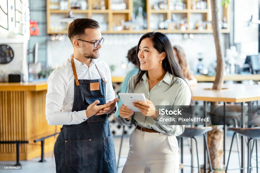 Managing a small business Male waiter and female manager using a digital tablet in a coffee shop. Food and drink business concept Small Business Stock Photo