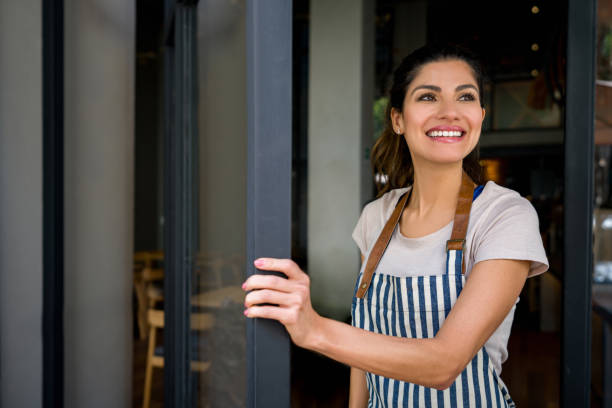 istock Happy waitress opening the doors of a restaurant and smiling 1341912075