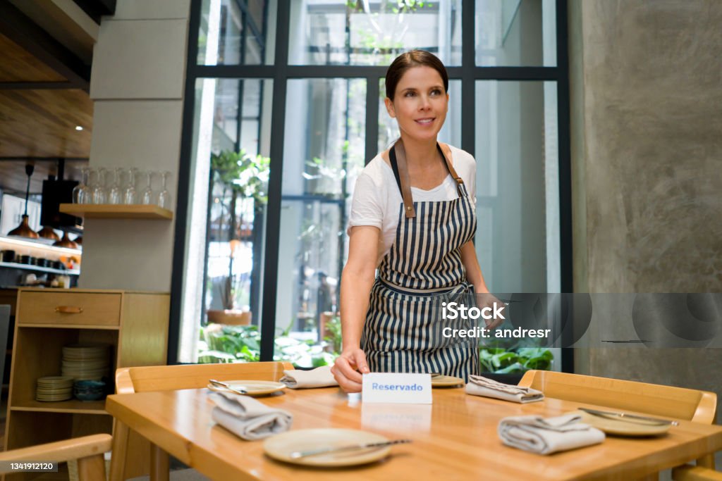 Waitress putting a reserved sign on a table at a restaurant Happy waitress putting a reserved sign on a table while working at a restaurant - food service concepts Making a Reservation Stock Photo