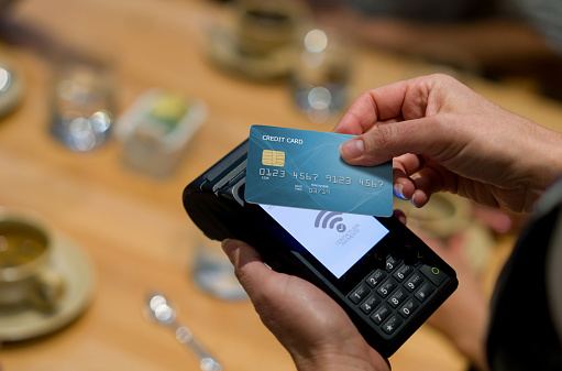 Close-up on a customer at a restaurant making a contactless payment - technology in small business concepts. **DESIGN ON CREDIT CARD BELONGS TO US**