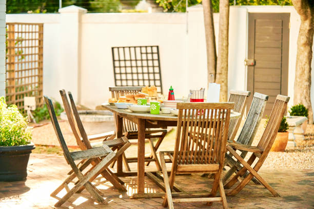 A beautifully crafted wooden table accompanied by a set of folding green chairs, all meticulously arranged on a paved area, ideal for enjoying outdoor dining experiences