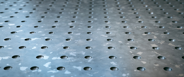 Extreme close-up on a dirty metallic surface floor background with drilled holes and diminishing perspective. Wide horizontal composition.