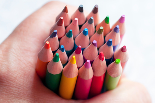 multi-colored sharpened pencils in a person's hand. The concept of stationery, school supplies, drawing and motor skills development in children.
